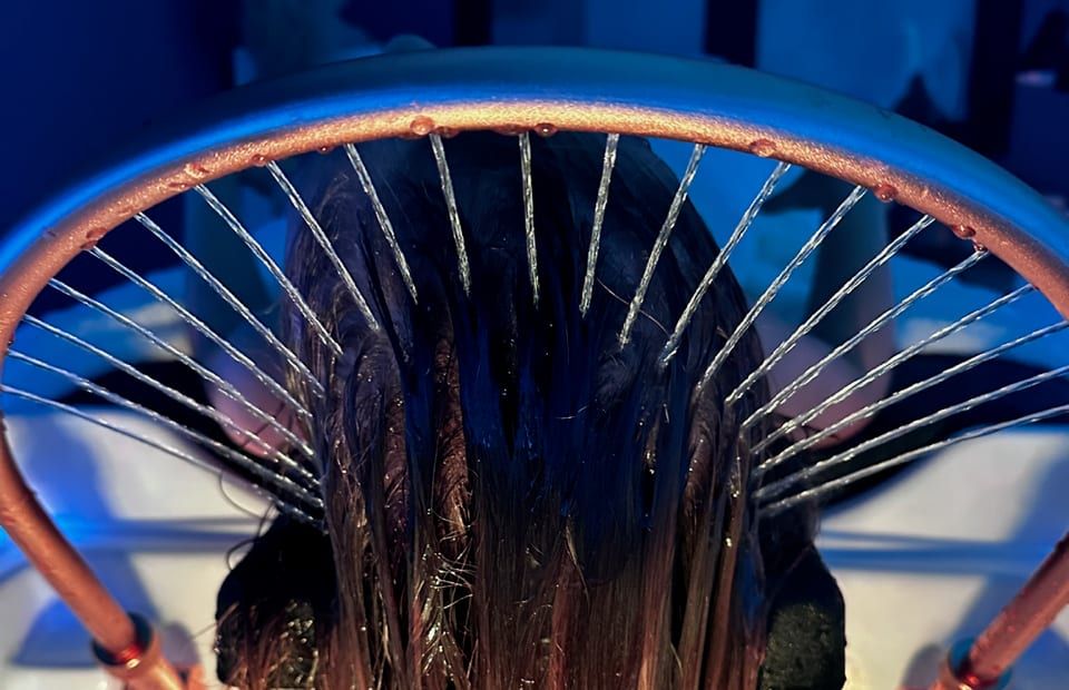 Arche head spa cuivrée diffusant de fins jets d’eau sur une chevelure, dans une lumière bleutée
